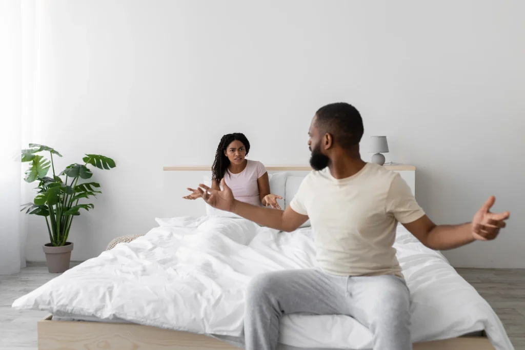 Un homme et une femme qui se dispute dans la chambre. La femme est dans le lit. L'homme est assis au bord