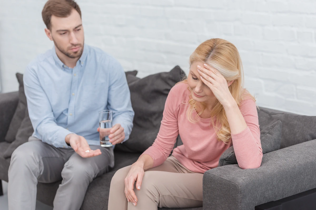Une femme en larme assise à côté d'un homme qui lui tend un verre d'eau