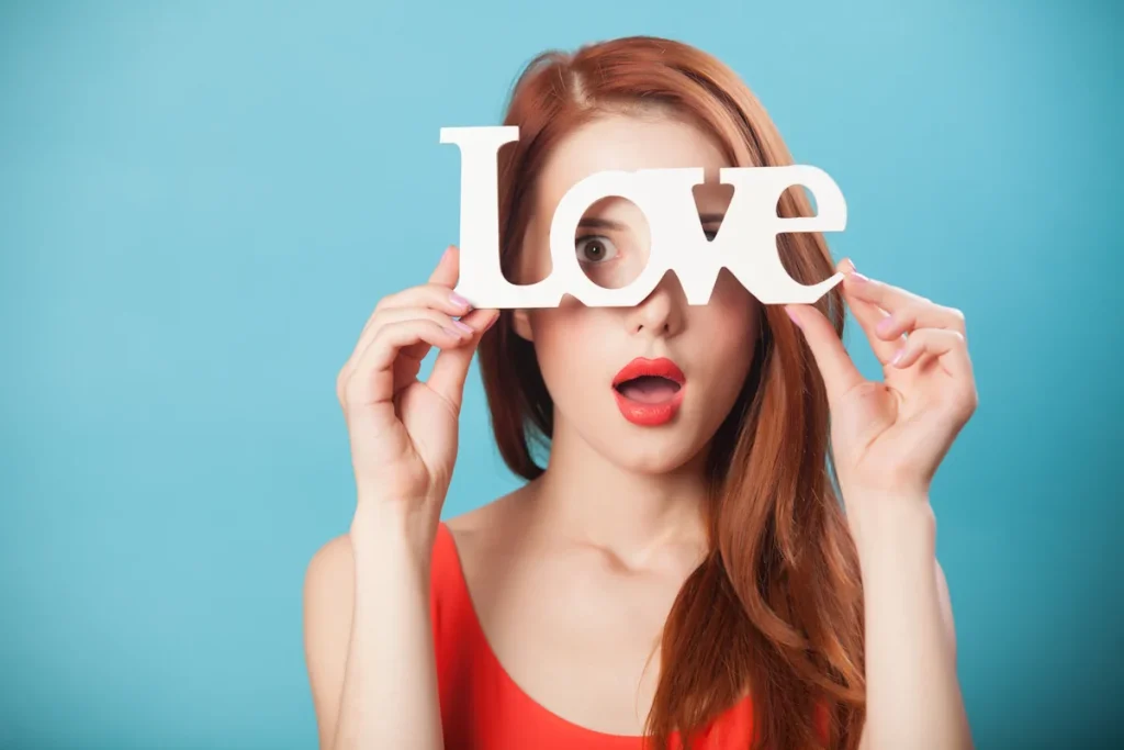 Une femme en robe rouge qui tient le mot LOVE dans ses mains face à ses yeux