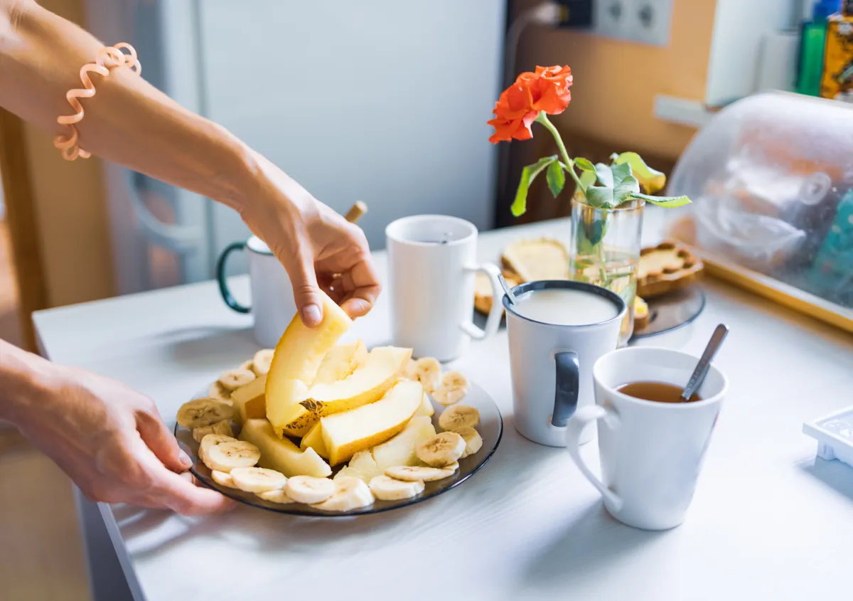 Une personne qui prend un morceau de fruit dans une assiette posée près de plusieurs tasses de boissons chaudes