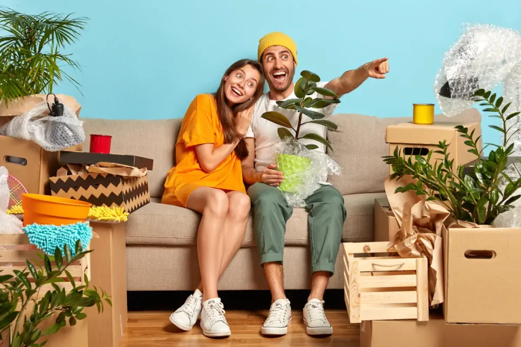 Un jeune couple sur un canapé qui tient une plante dans un pot entouré de carton