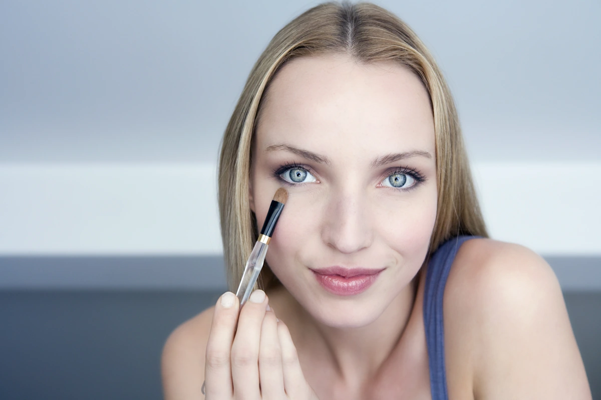 Une jeune femme aux yeux bleus qui se maquille légèrement