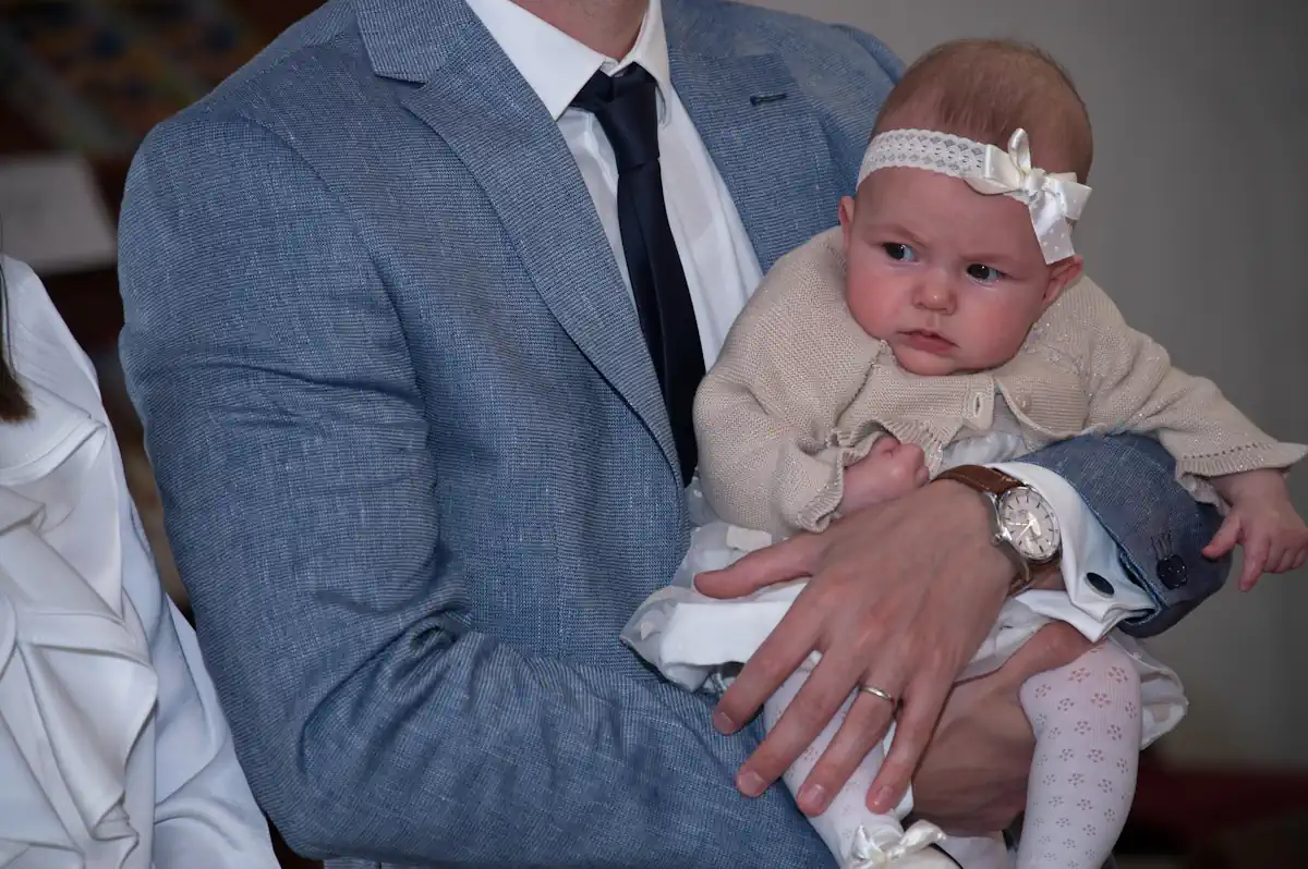 Un homme en costard cravate qui tient un bébé avec un nœud blanc sur la tête